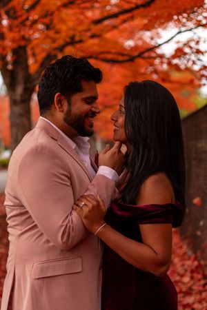 Happy couple sharing a tender moment together under brilliant red autumn maple trees.
