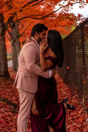 Couple sharing a passionate kiss surrounded by vivid red fall foliage and fallen leaves.