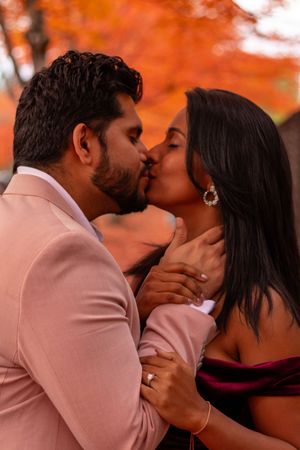 Close-up of newly engaged couple kissing with engagement ring visible against autumn backdrop.