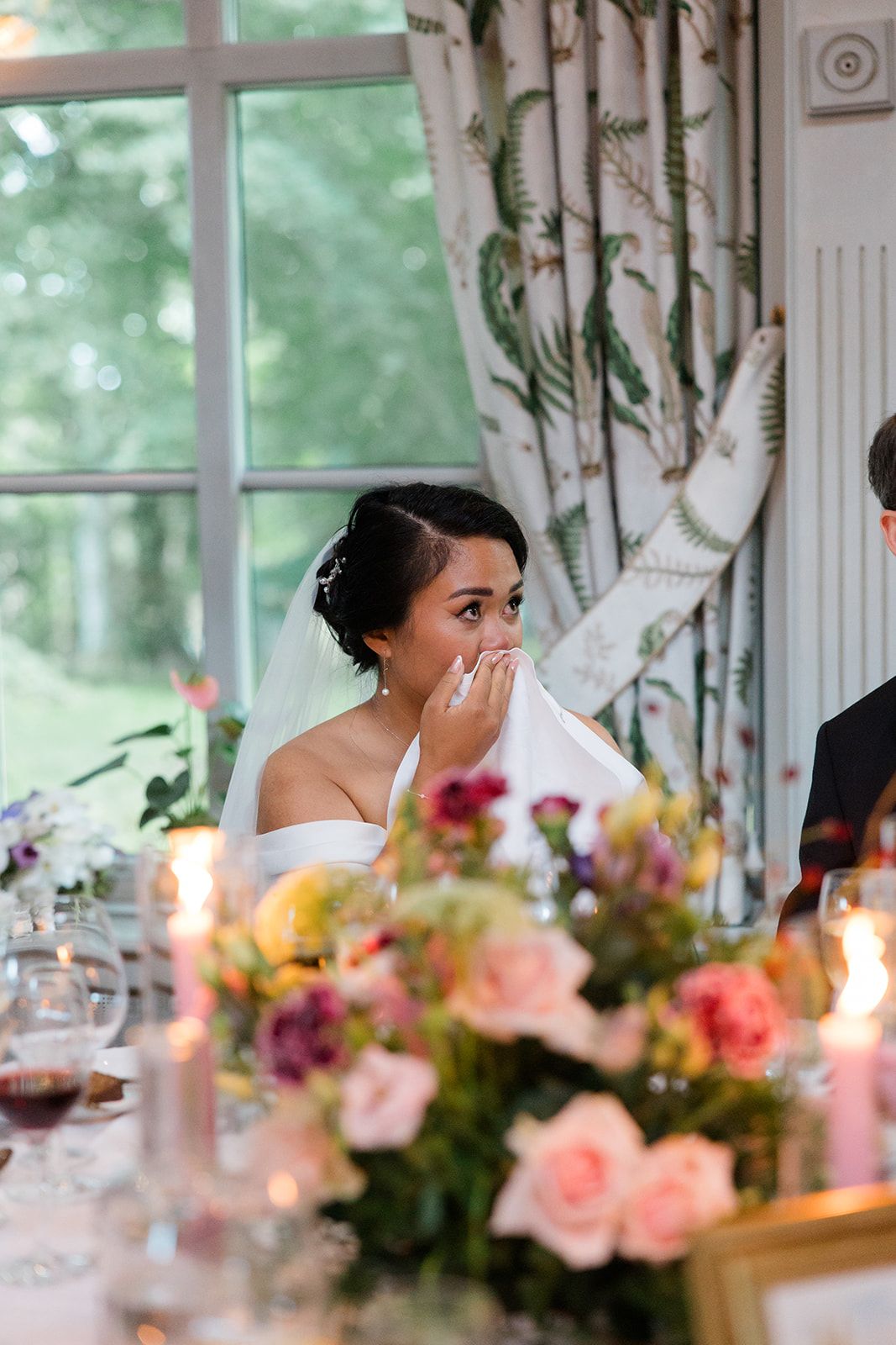Black and white candid wedding reception photo showing bride in veil and groom seated at table during celebration.