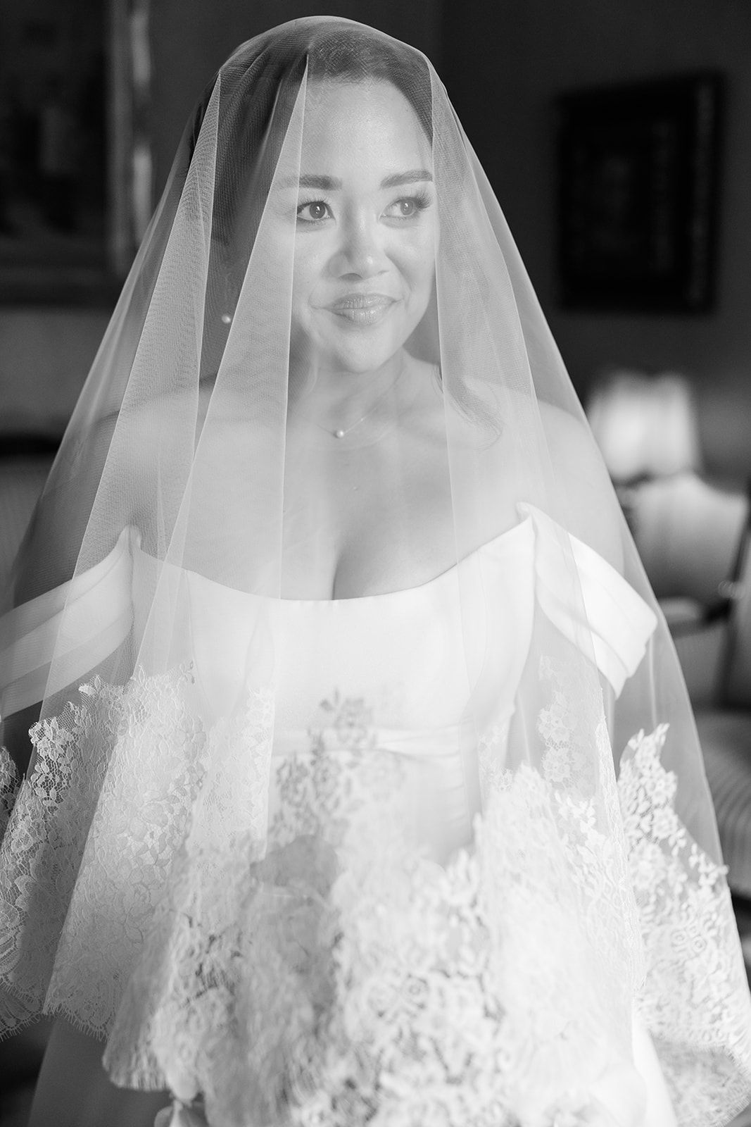 A bride wearing a delicate lace veil smiles in a series of black and white wedding portraits.