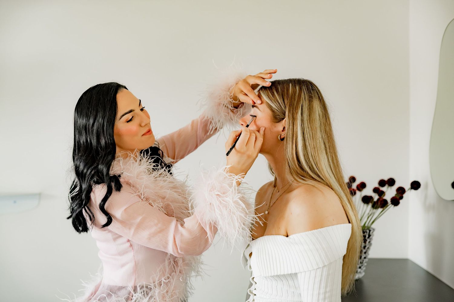 Two women in white sweaters sharing a playful moment while posing together in a bright room.