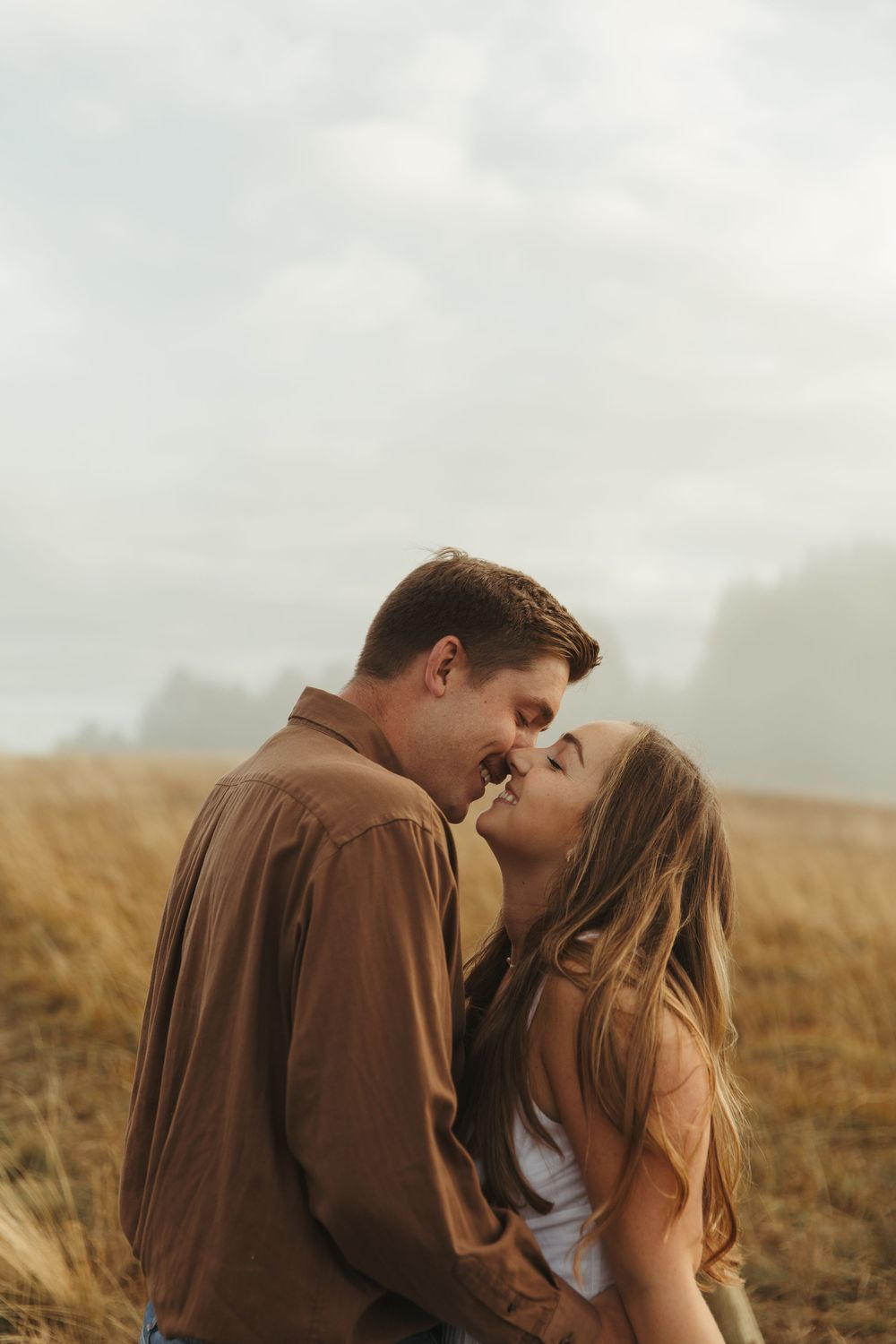 A couple shares a romantic kiss in a golden wheat field on an overcast day.