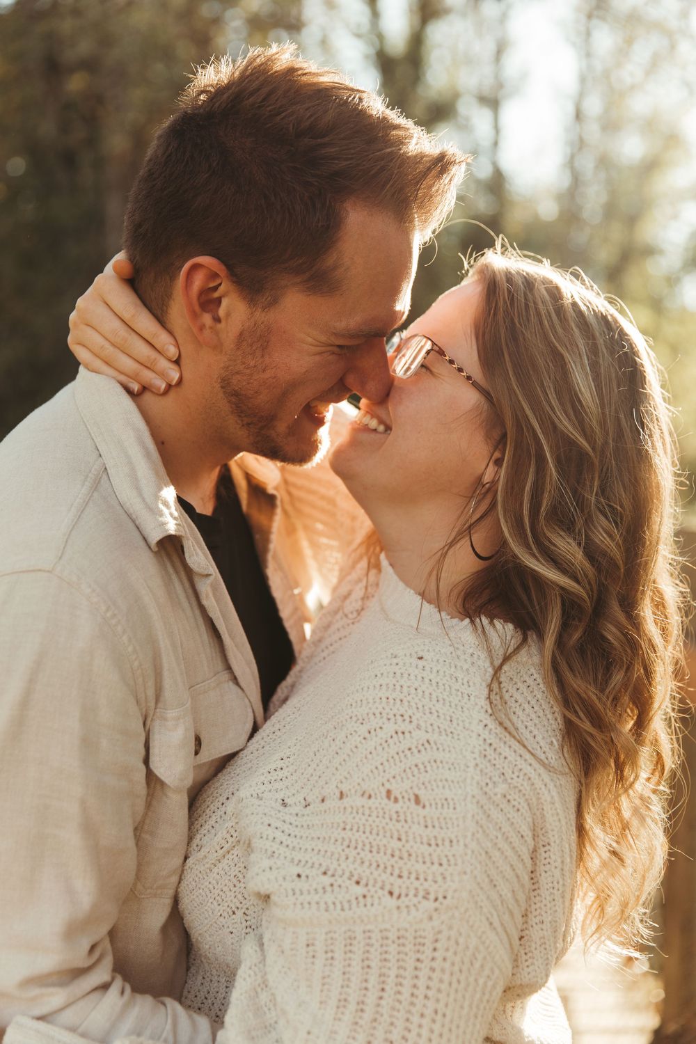 A romantic couple shares intimate kisses in golden sunlight while wearing white and cream colored clothing.