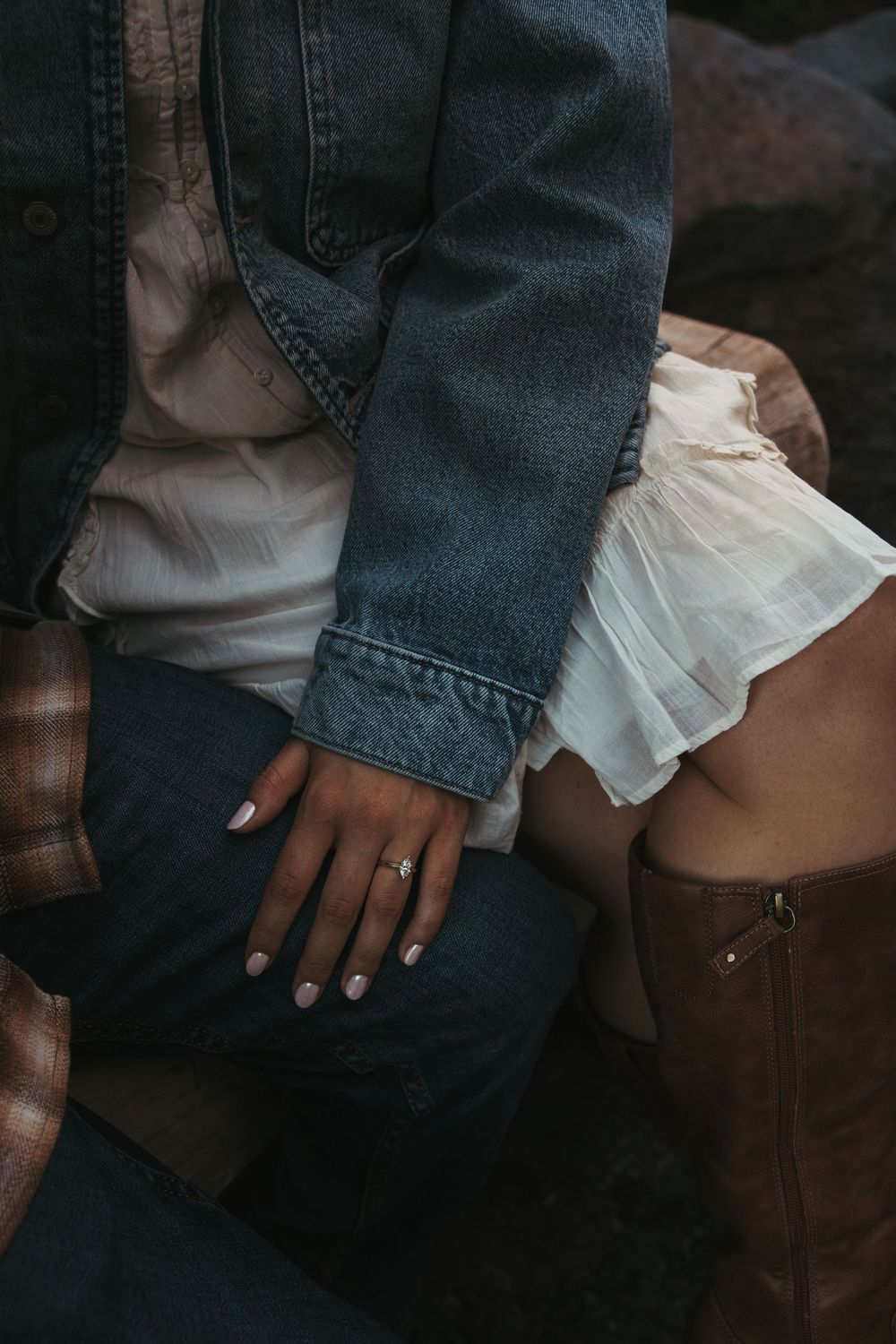 Close-up of couple sitting together, woman wearing engagement ring, white tulle skirt, brown boots, man in denim jacket.