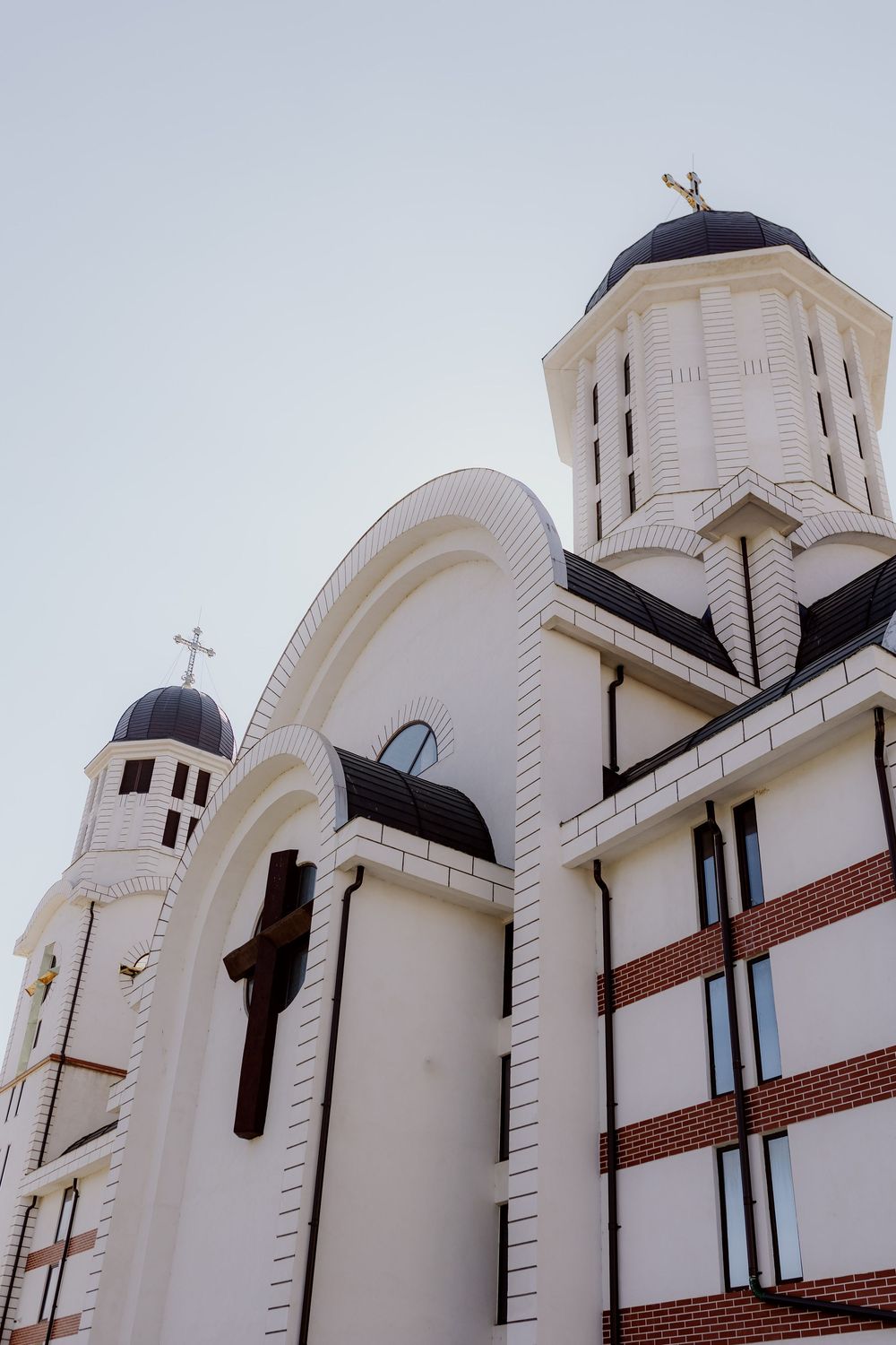 White Orthodox church exterior with ornate towers and crosses against a pale blue sky.