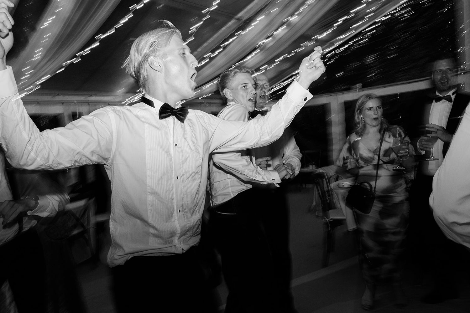 Wedding guests dance and celebrate on a dimly lit dance floor during an evening reception party.