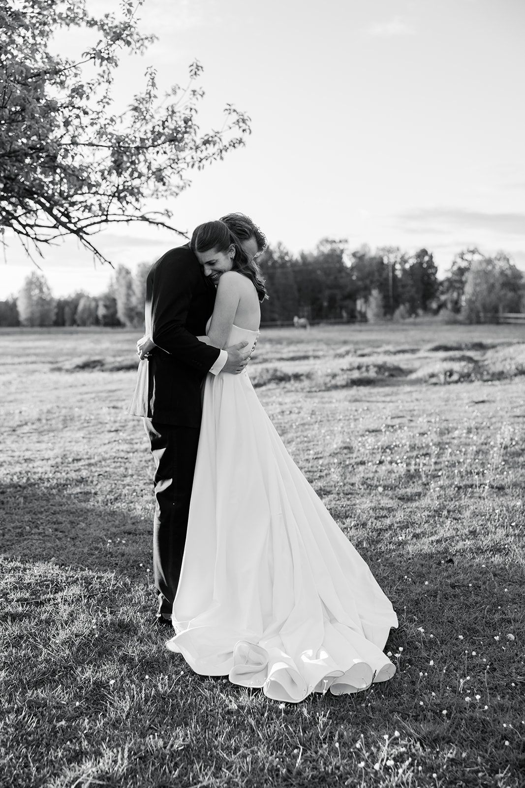 A black and white wedding photo series shows a couple embracing in a scenic outdoor field at sunset.