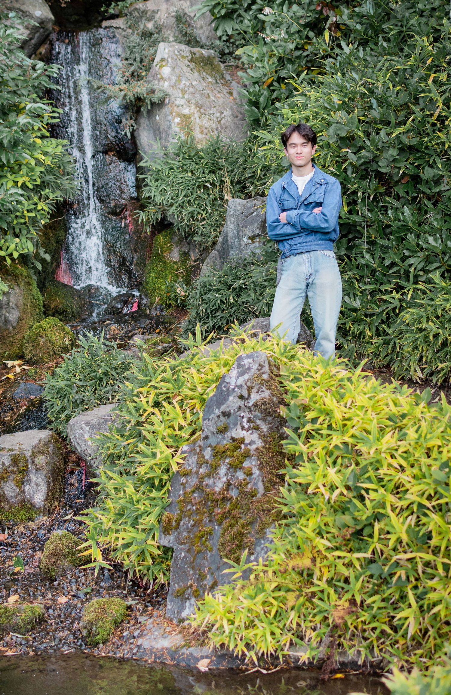High school senior posing near small waterfall and lush greenery at Kubota Garden in Seattle, Washington.
