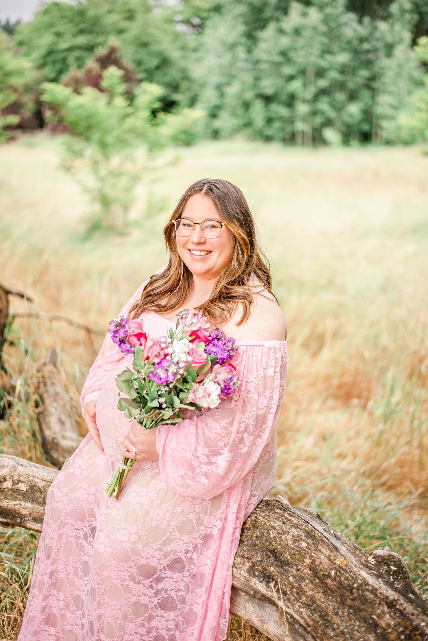 A romantic portrait session in a meadow featuring pink lace dress and vibrant purple flower bouquet against natural foliage.
