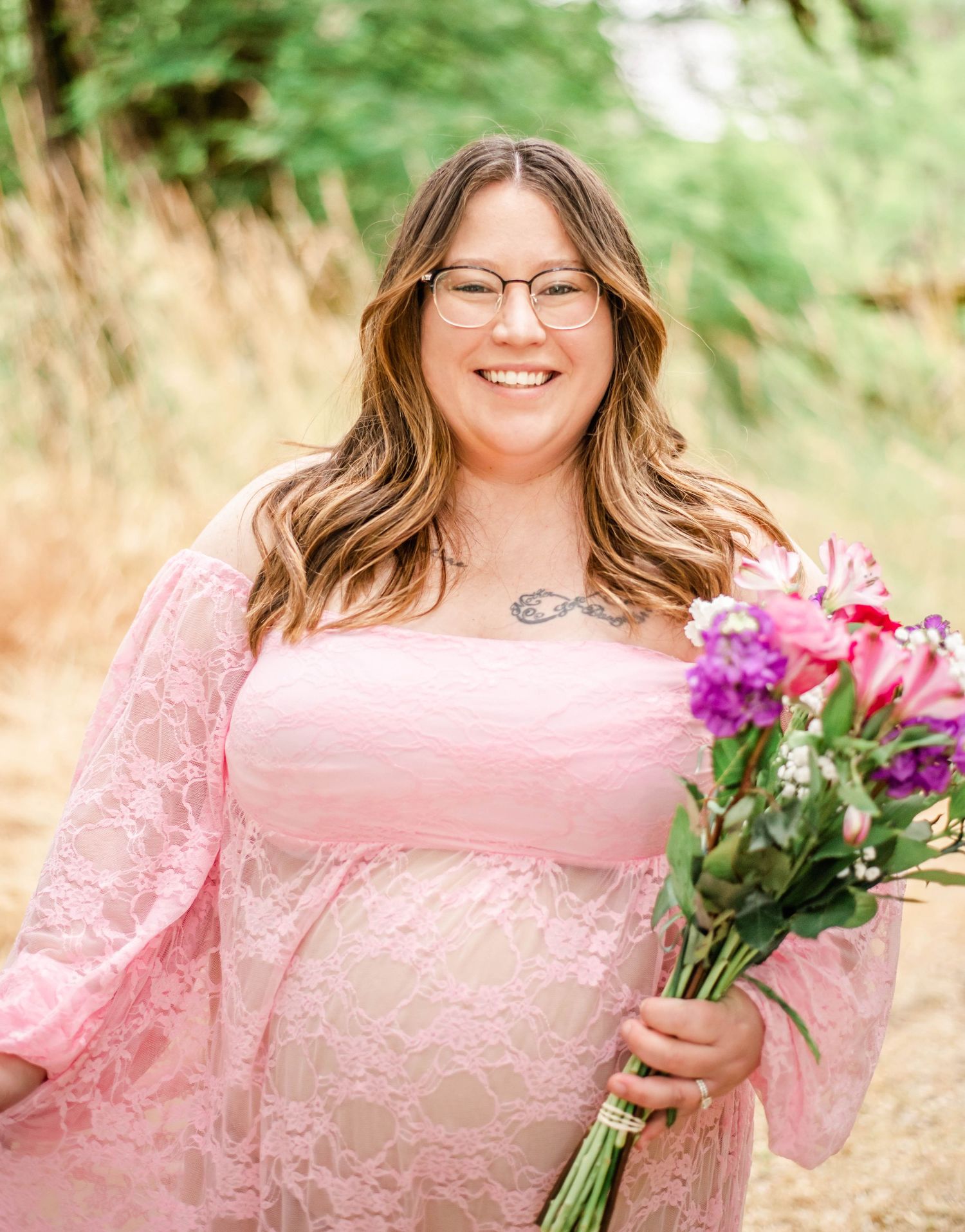 A joyful portrait in a pink lace dress holding a vibrant bouquet of flowers against a natural outdoor background.