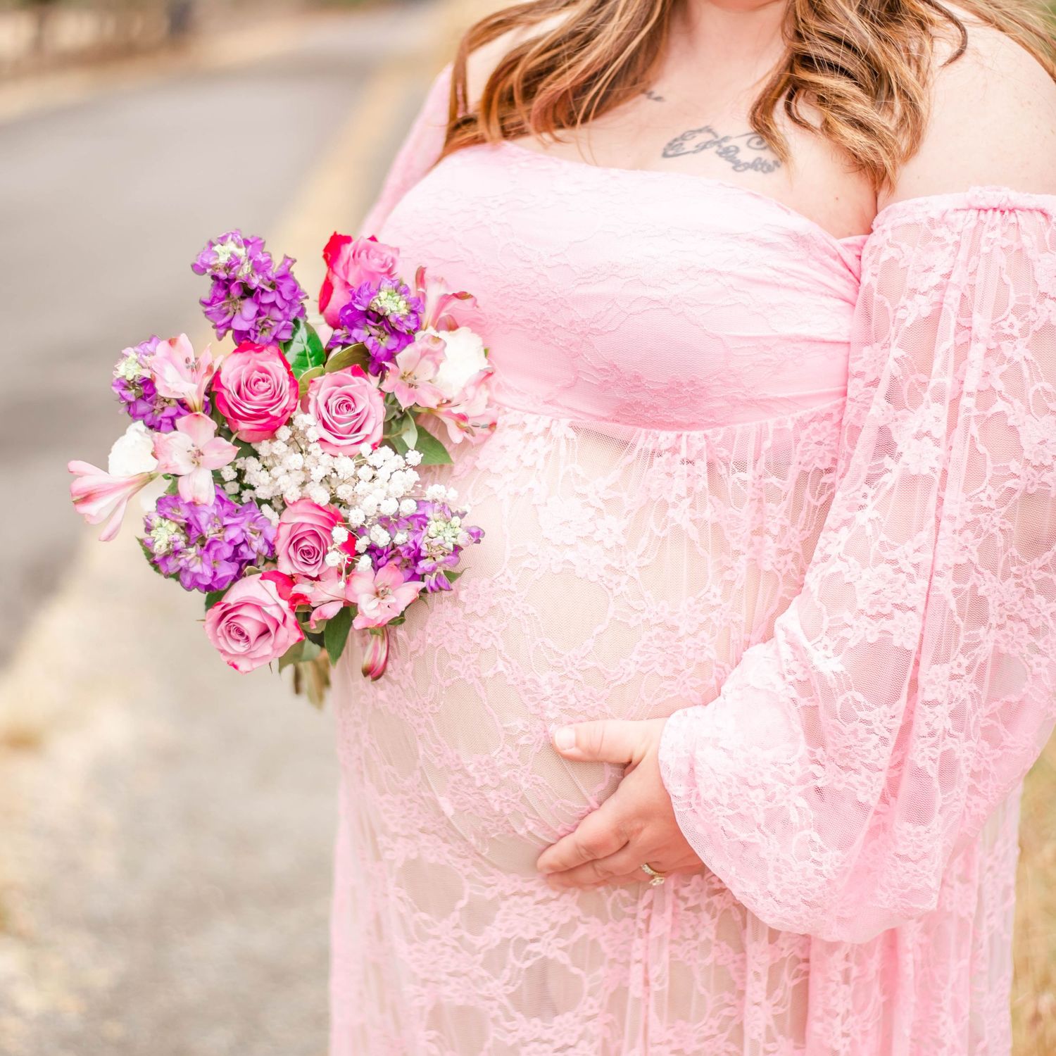 Pink floral bouquet held against a flowing pink lace dress during an outdoor maternity photography session.
