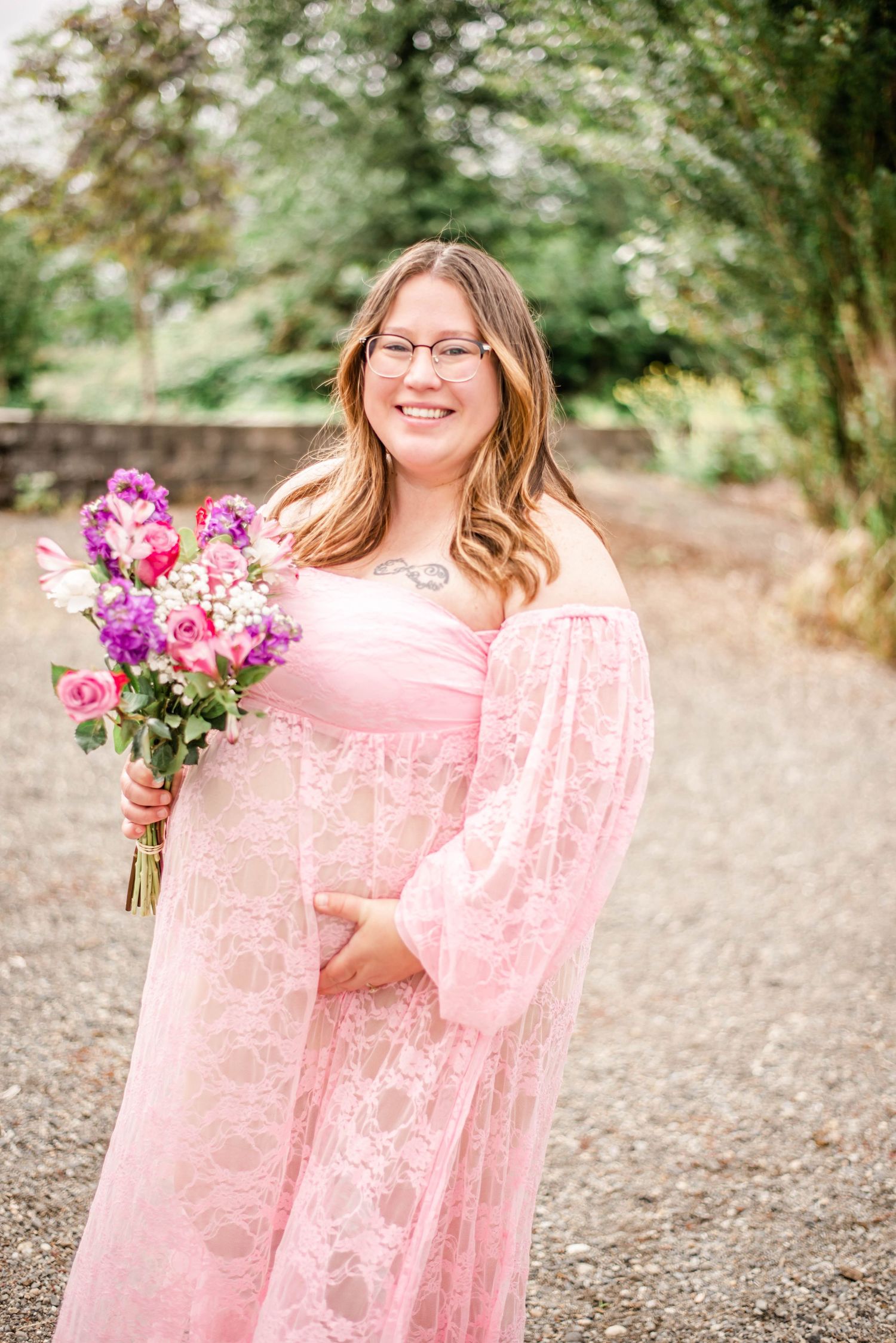 A person wearing a pink lace dress holds a vibrant bouquet of pink and purple flowers in an outdoor garden setting.