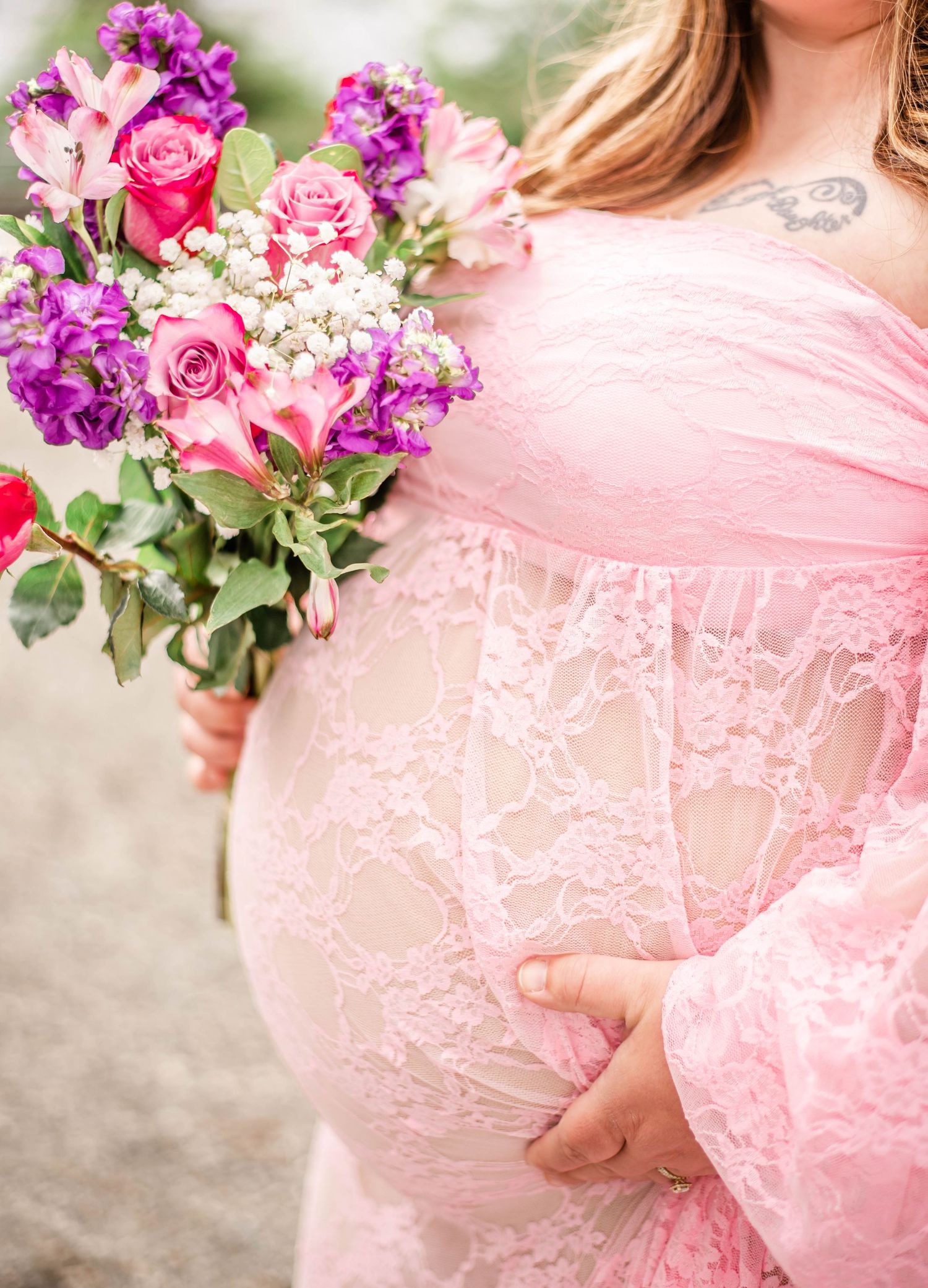 A delicate pink lace maternity dress with floral bouquet featuring purple and pink blooms against a soft background.