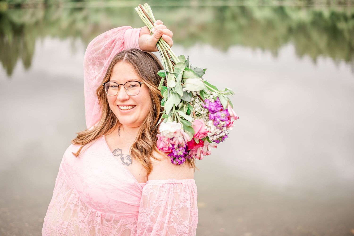 Portrait session in a pink dress with floral bouquet near a reflective pond.