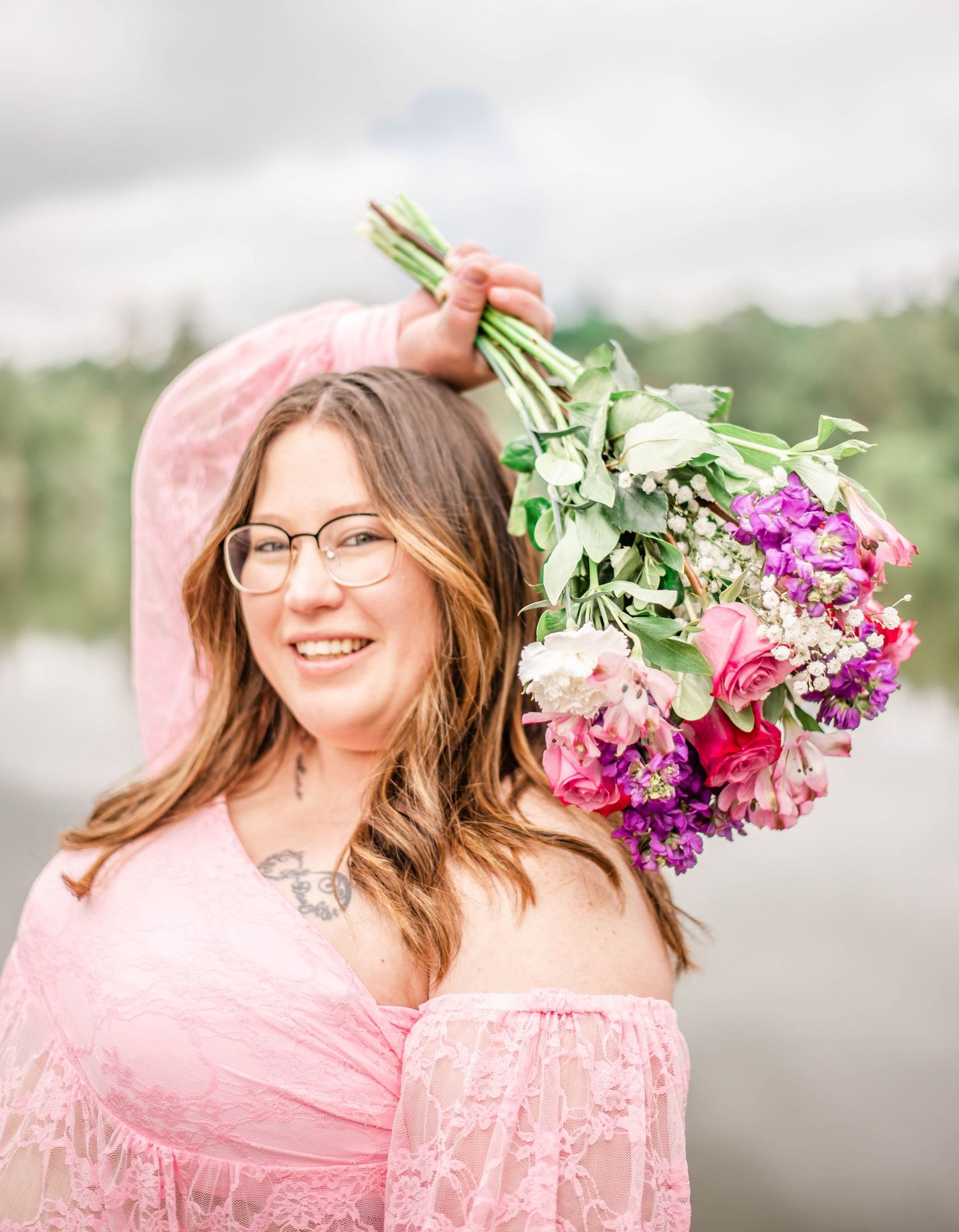 Maternity photo in pink dress holding elevated bouquet of pink and purple flowers.