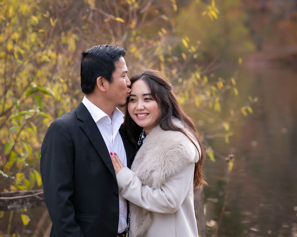 Couple sharing a tender moment by a reflective pond surrounded by golden autumn leaves. Holmdel Park NJ Monmouth County