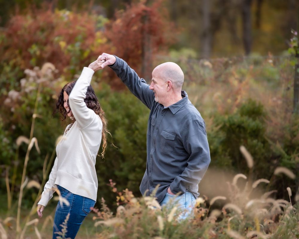 portrait of Couple dancing playfully in an autumn field, man spinning woman among golden fall grasses. Middletown NJ Monnouth County