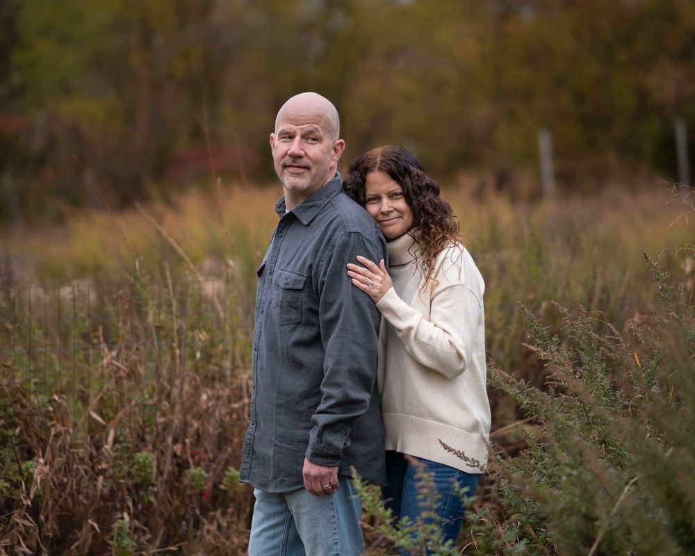 Couple standing close together in a fall meadow, woman resting hand on mans back outdoors. Poricy Park Middletown NJ Monnouth County