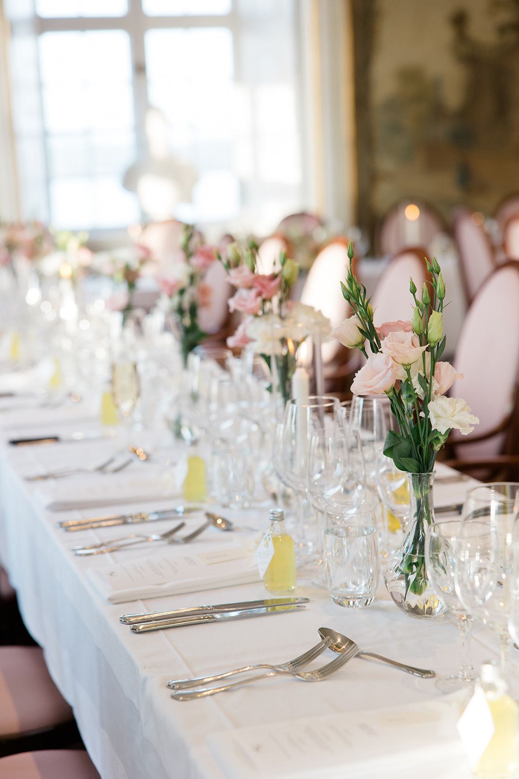 Elegant wedding reception tables set with white linens, crystal glasses, and delicate floral centerpieces in pink and white.