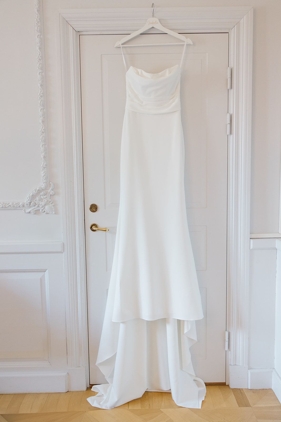 Five white wedding dresses hanging on hangers against a white wall showing different styles and silhouettes.
