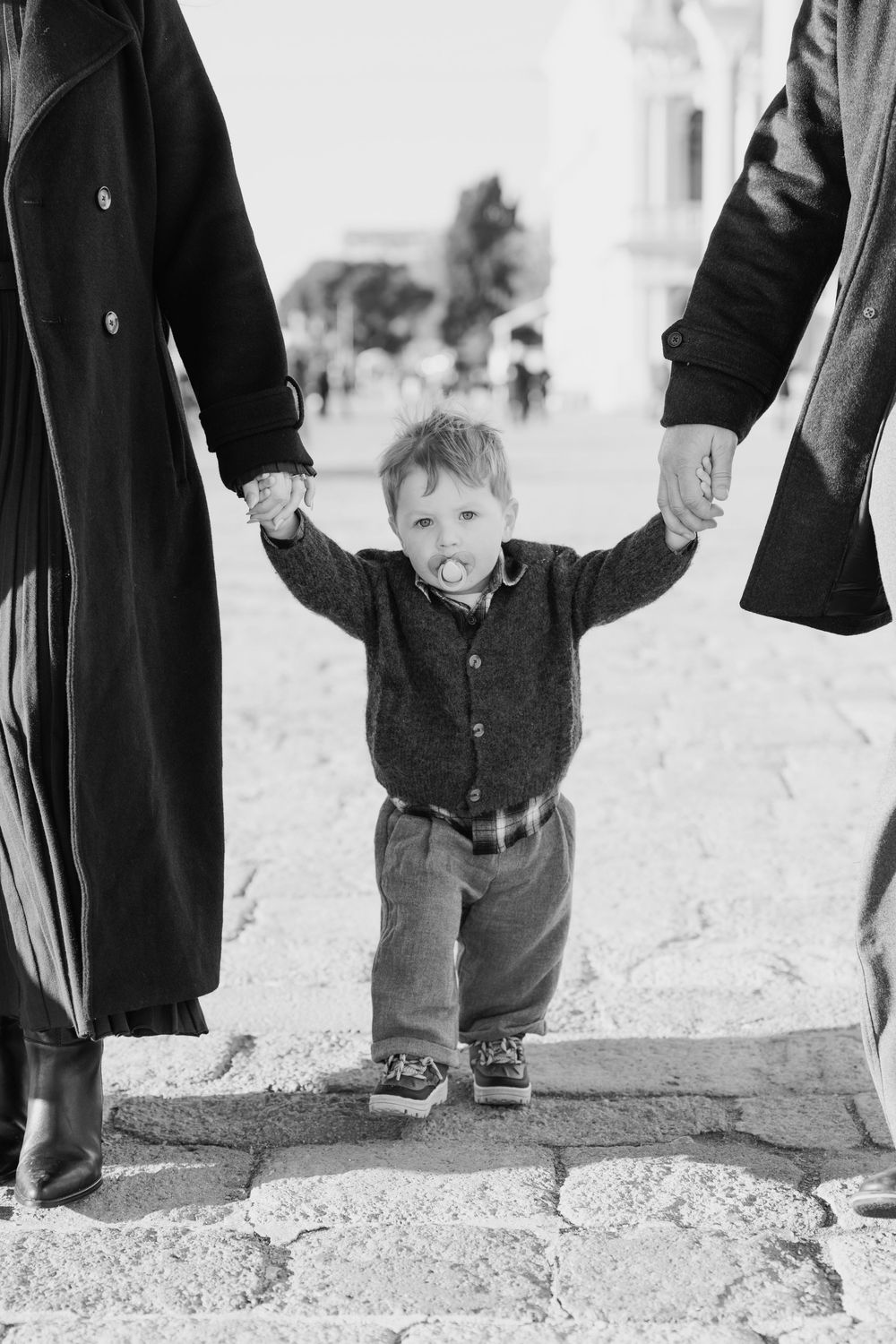 A vintage black and white photograph showing people's legs and a small child standing on a dirt ground. Venice Family photographer.