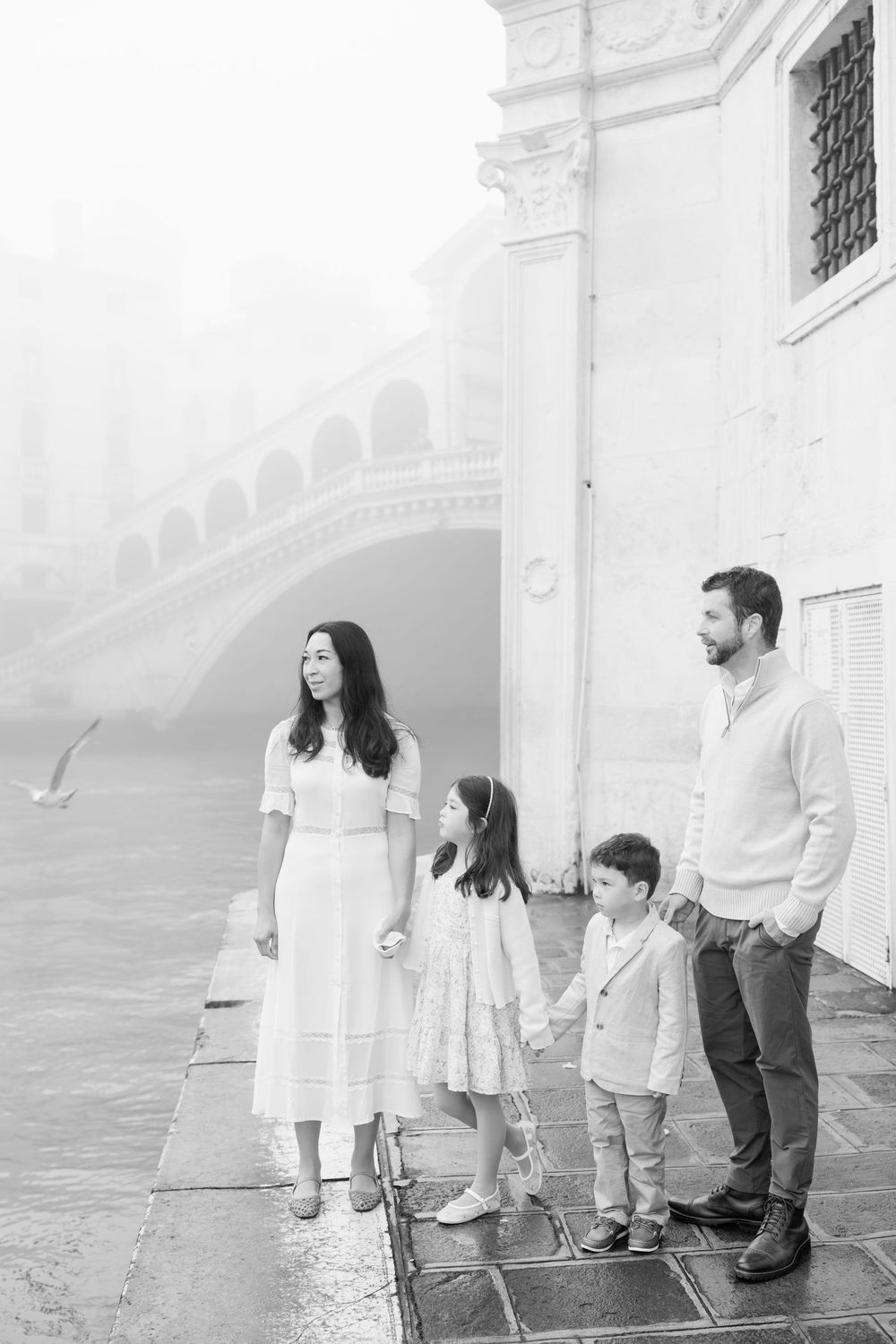 Family wearing coordinated white and gray outfits poses together against white building exterior.