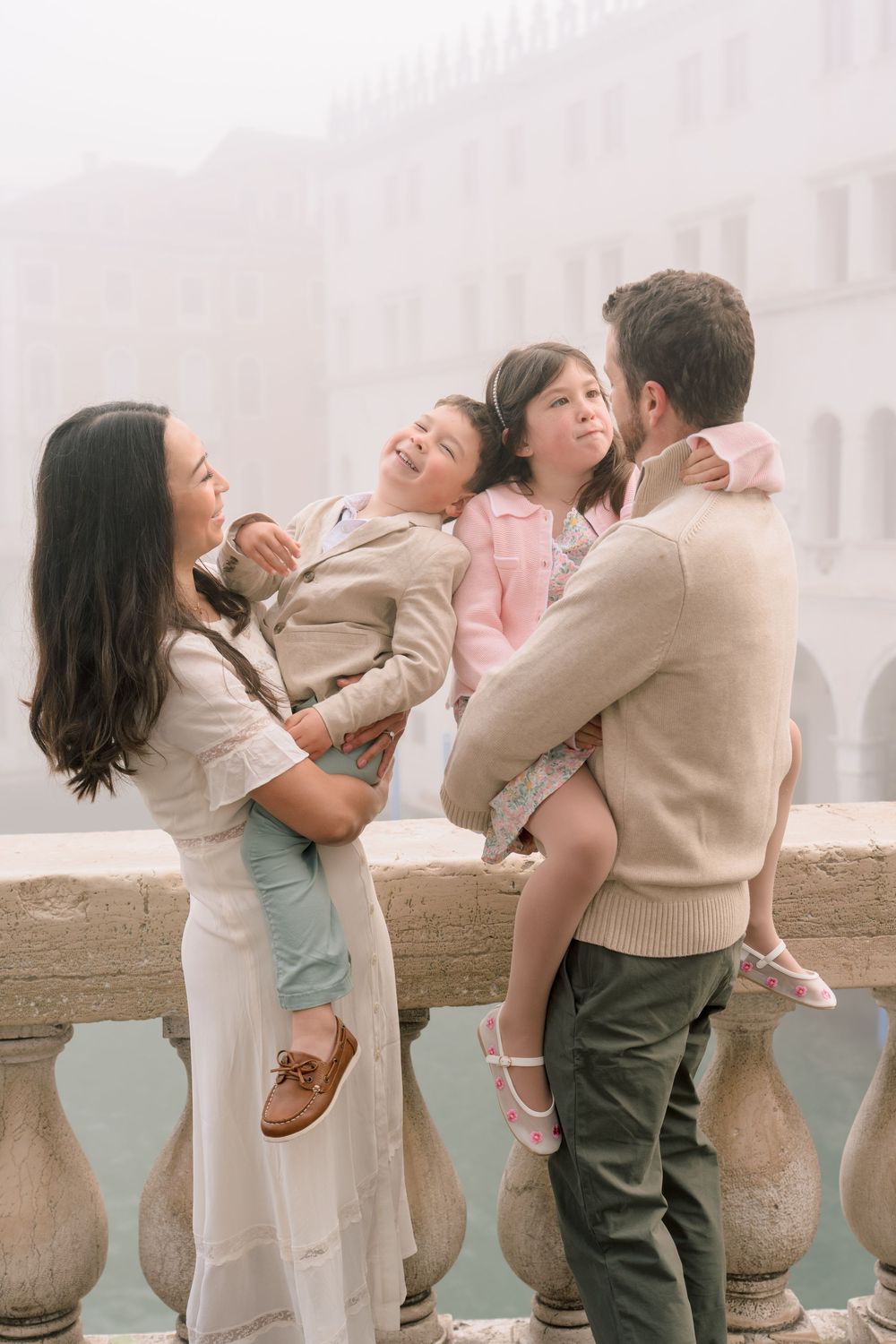 Family sharing joyful moments together while posing along a stone balustrade in coordinated neutral outfits.