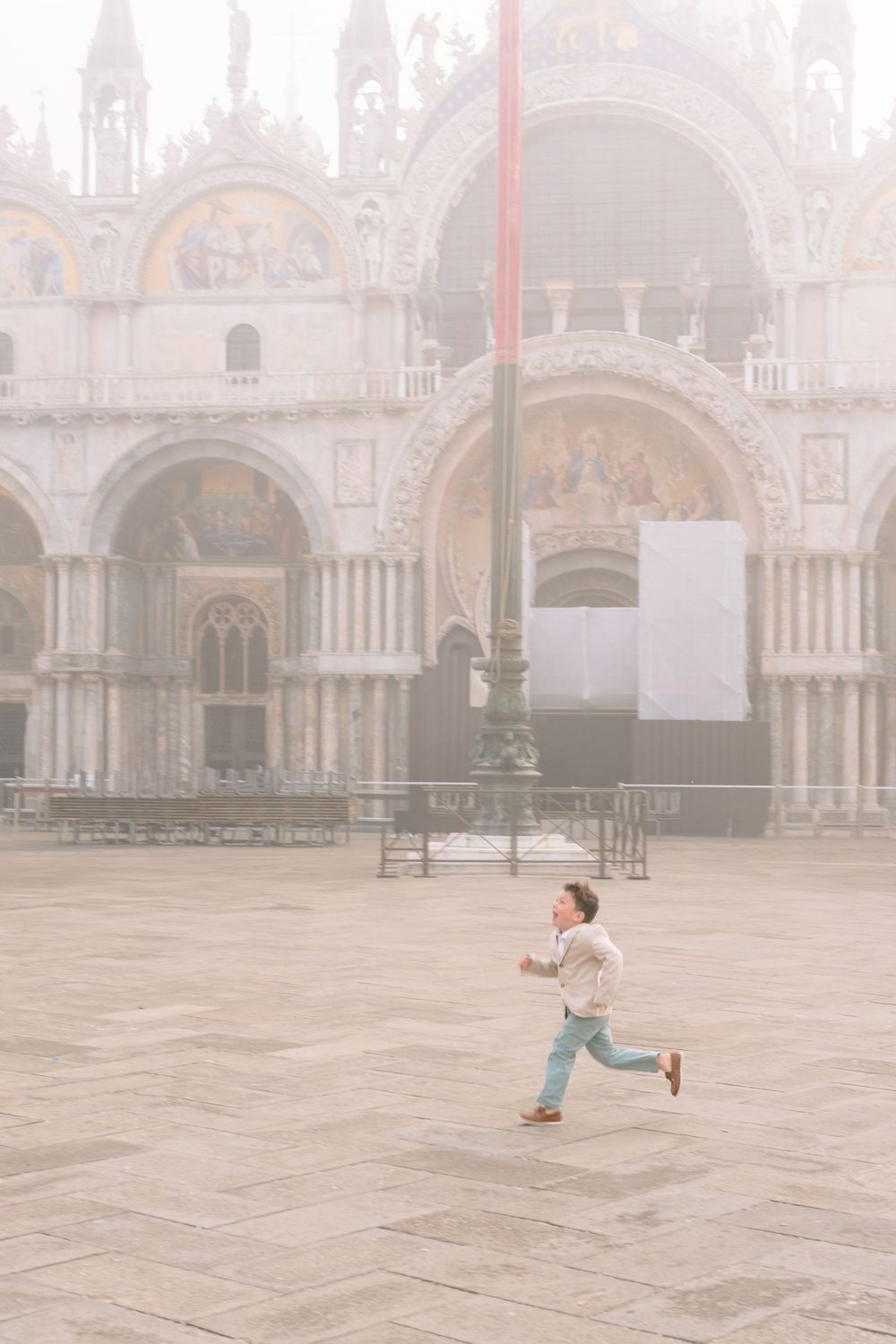 A young child runs across the misty Piazza San Marco in Venice with Saint Mark's Basilica in the background.