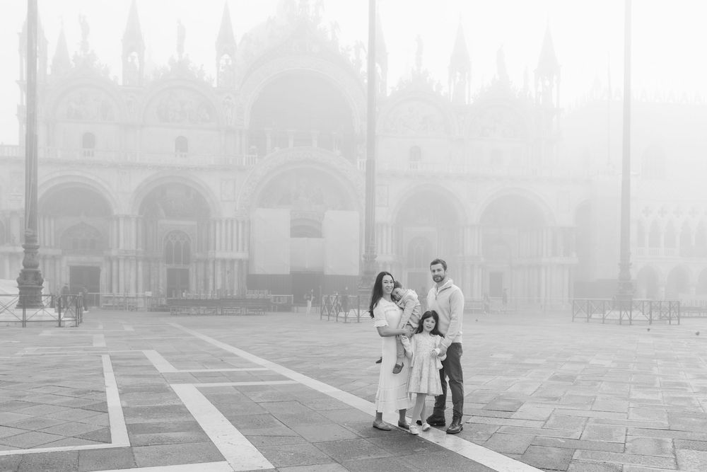 People walking through a misty park on a foggy day with buildings and trees visible in the background.