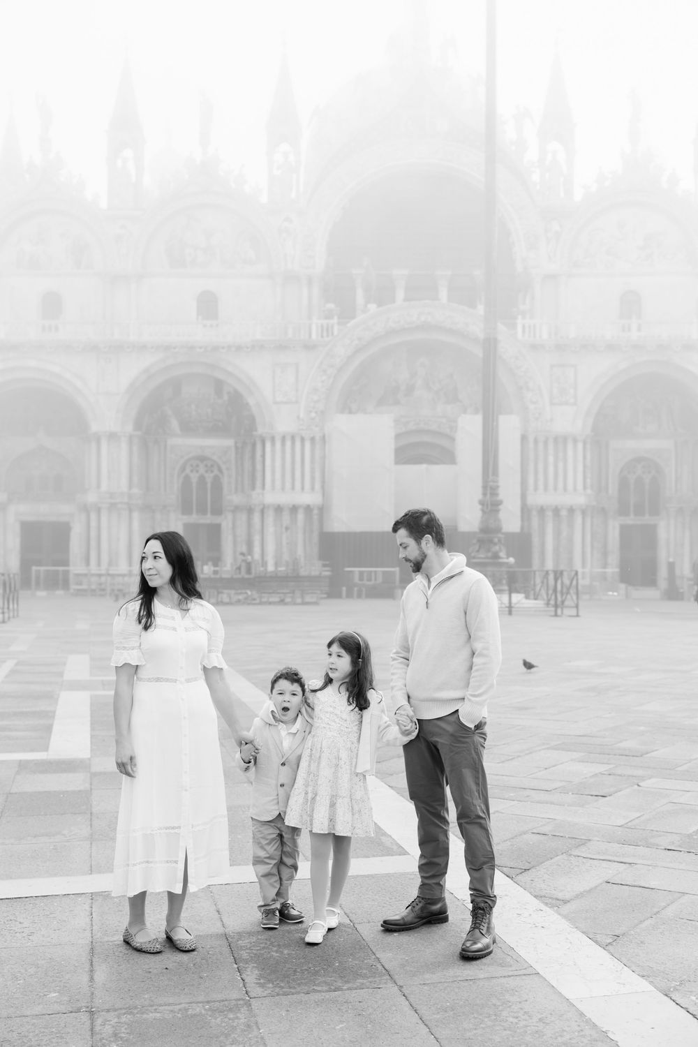 A family in coordinated white outfits walks together through the misty morning in Venice's St. Mark's Square.