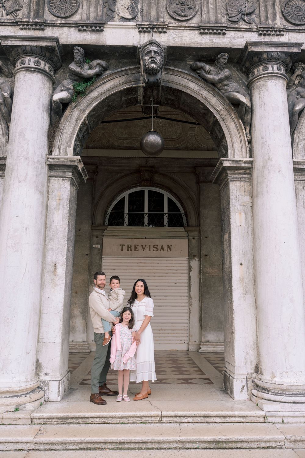 Elegant engagement photo session captured in a historic colonnade with white stone pillars and arched architecture.