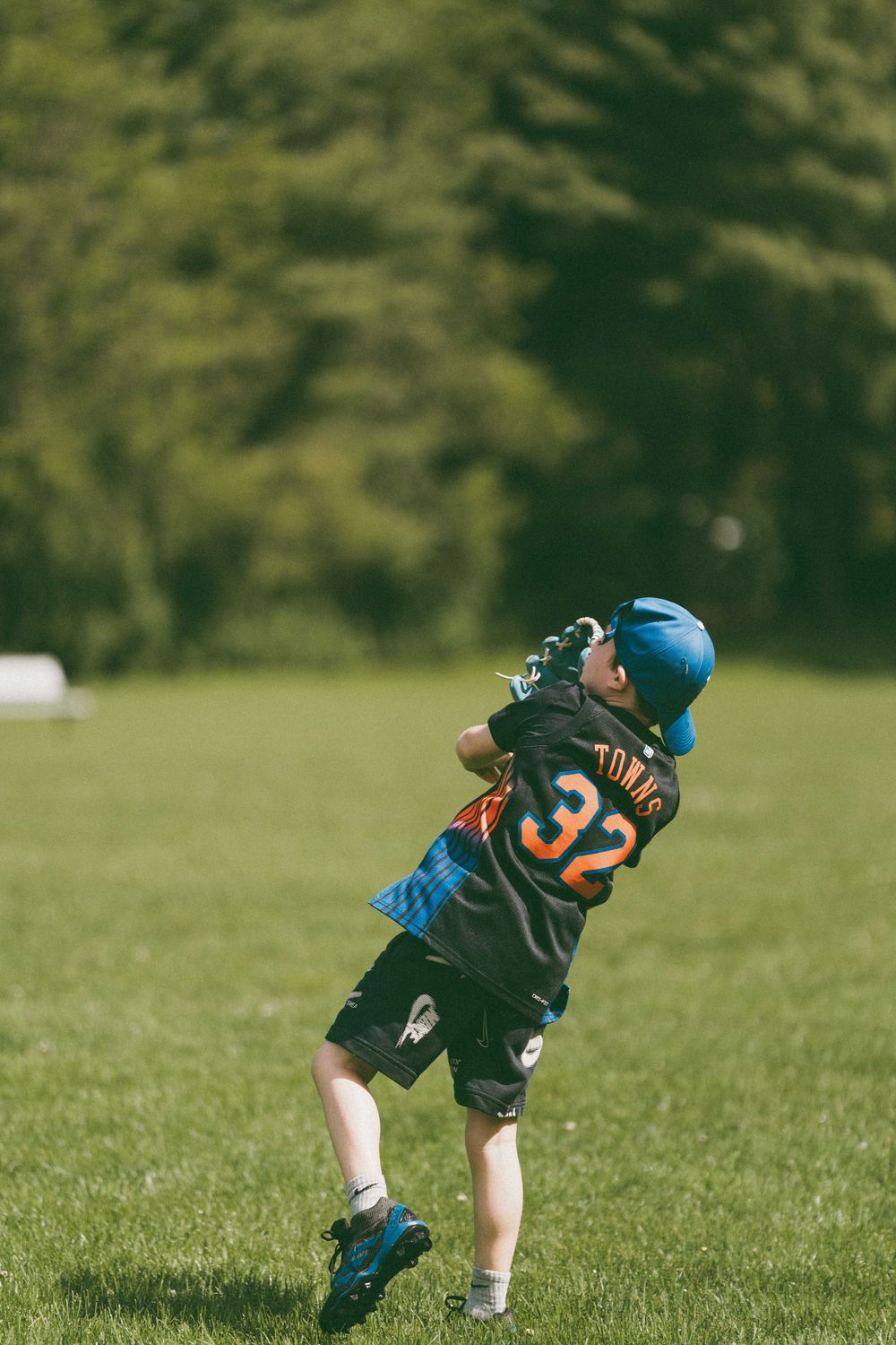 Young baseball player wearing number 32 jersey and blue helmet swings bat during little league game on green field.