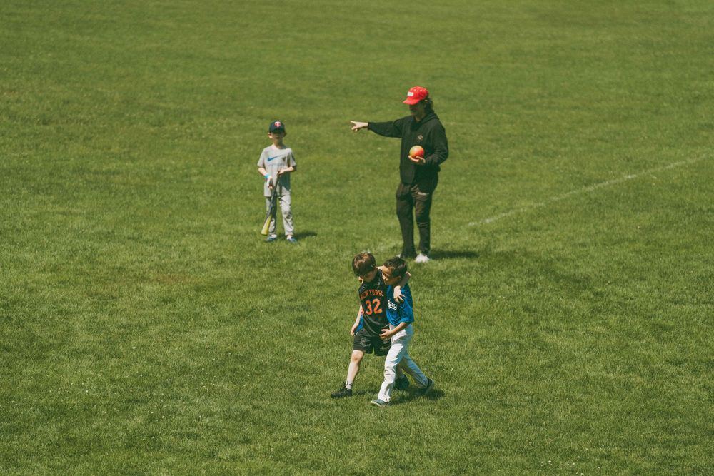 Children playing soccer on a green field with a coach in a red hat directing the young players during practice.