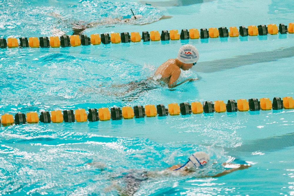 Competitive swimmers race in an indoor pool with green and yellow lane dividers during a swimming competition.