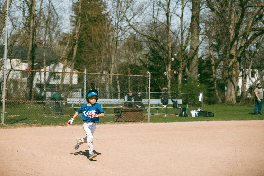Young boy in blue baseball uniform running bases on a dirt field during a youth little league game outdoors.
