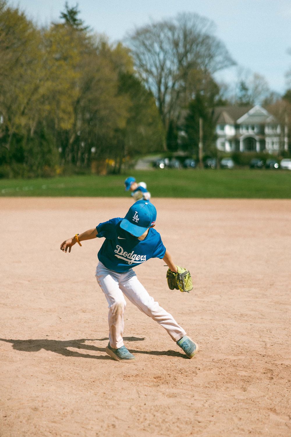 Young Dodgers player in blue uniform fielding on a sandy baseball diamond during a sunny spring game.