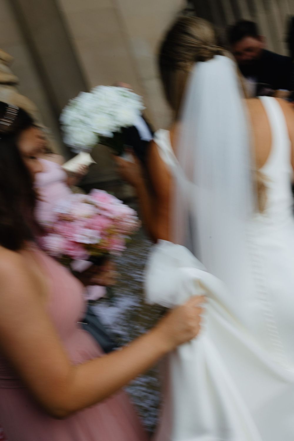 A blurred artistic shot of a bride in white dress and bridesmaid in pink holding bouquets during a wedding ceremony.