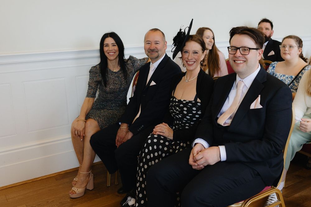 A group of guests in formal attire seated together at what appears to be a wedding or special event celebration.