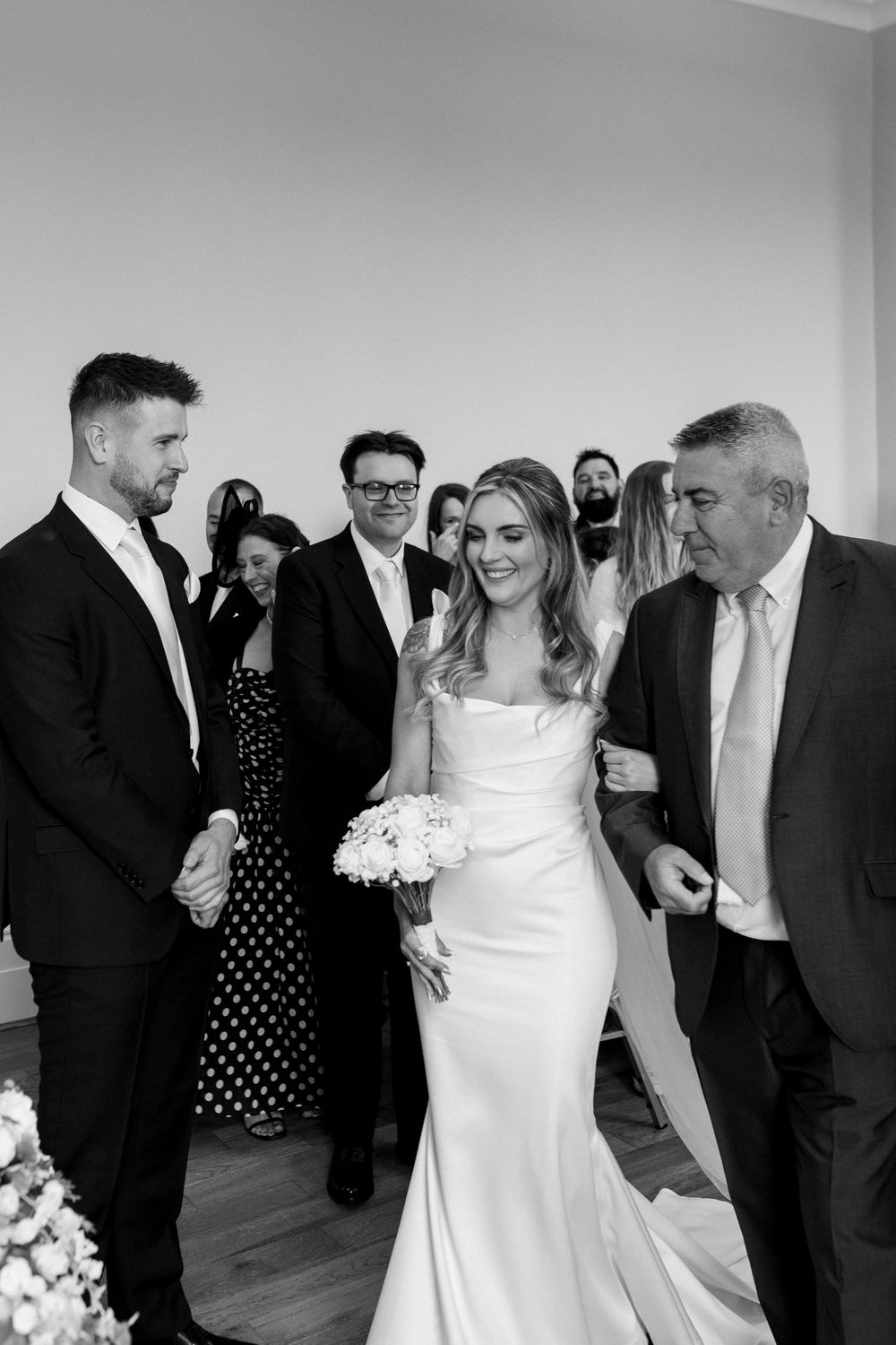Black and white wedding photo series showing candid moments between a bride in white dress and wedding party guests.