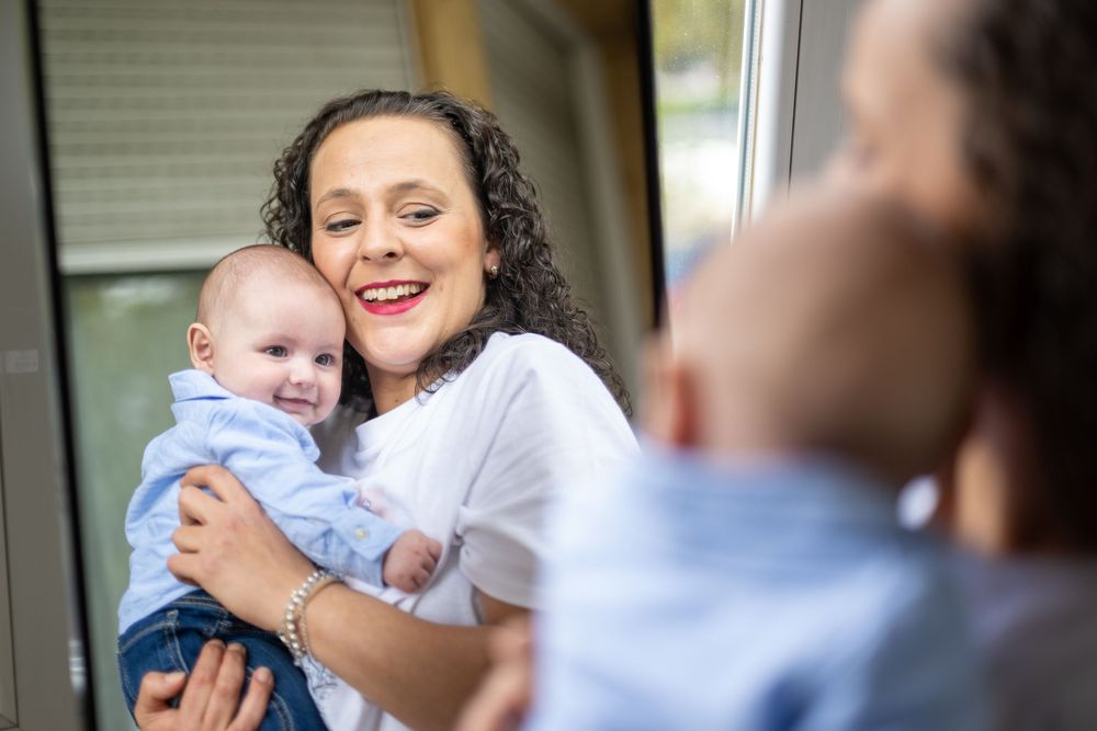 A tender moment between parent and baby as they share joyful smiles and cuddles in a bright indoor setting.