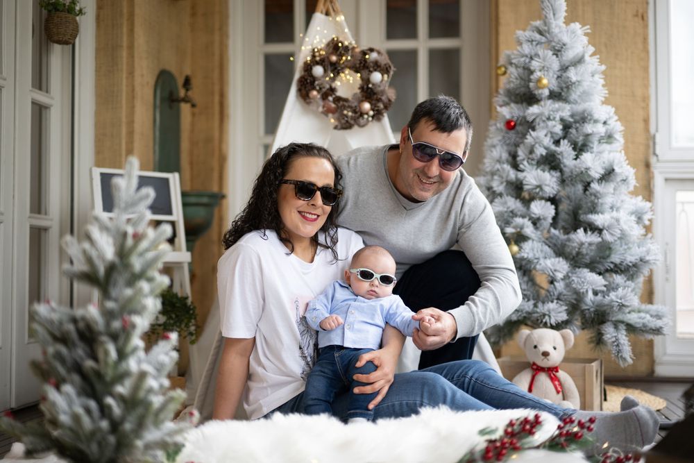 A family enjoys a cozy winter moment together near a flocked Christmas tree in a festive holiday setting.