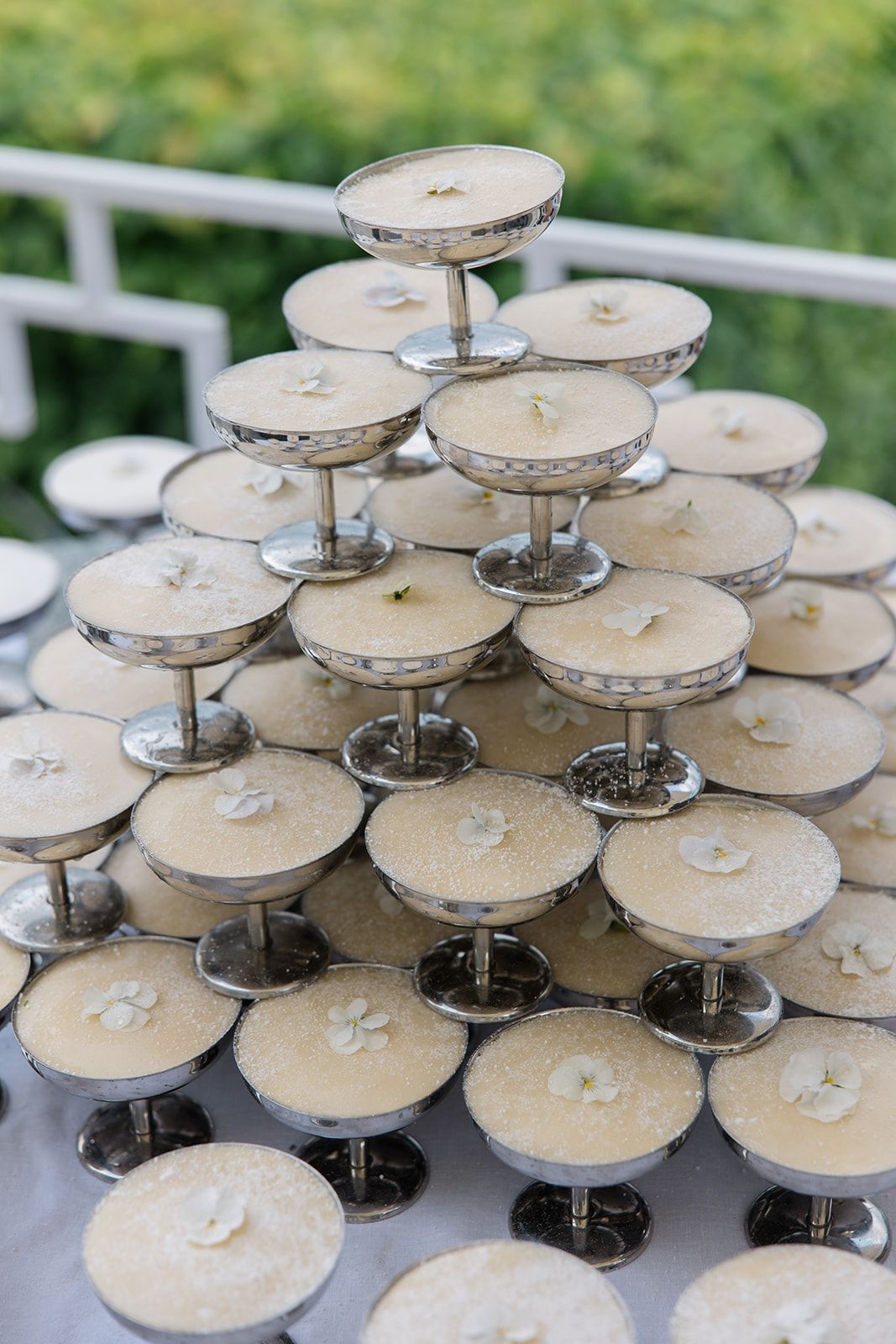 Multiple tiers of white wedding cupcakes displayed on silver stands at an outdoor reception.
