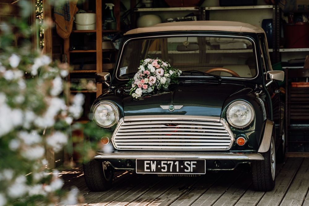 Classic black vintage car adorned with wedding flowers parked in front of a rustic building.