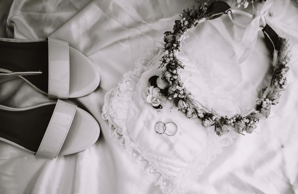 A series of elegant wedding detail shots in black and white showing rings, floral crown, and satin ribbons.