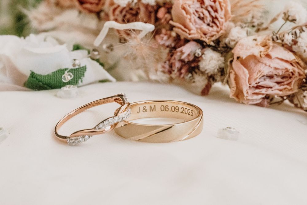 Delicate rose gold engagement ring with diamonds nestled among dried pink flowers and petals on white surface.