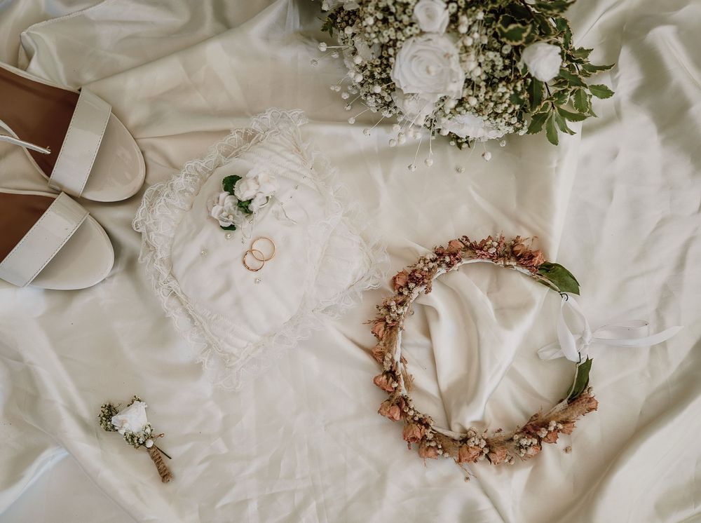 A collection of delicate floral crowns and wedding accessories arranged on white fabric with greenery accents.