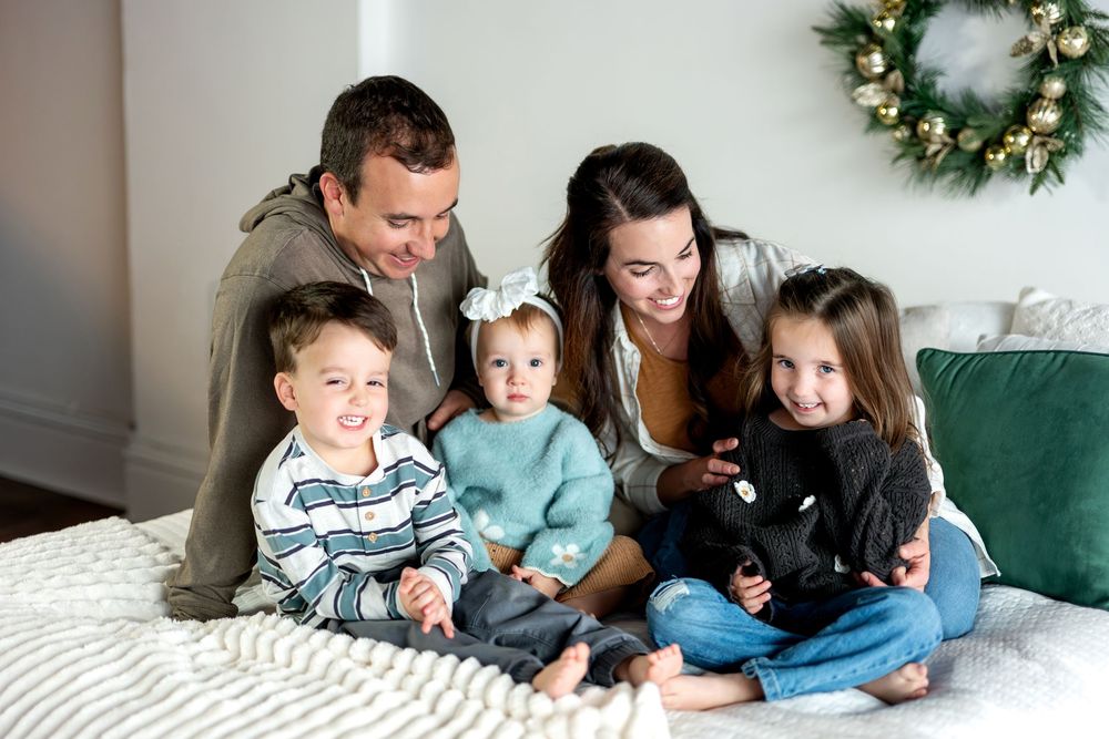 Joyful family of five sitting closely together on a bed with Christmas holiday decorations.