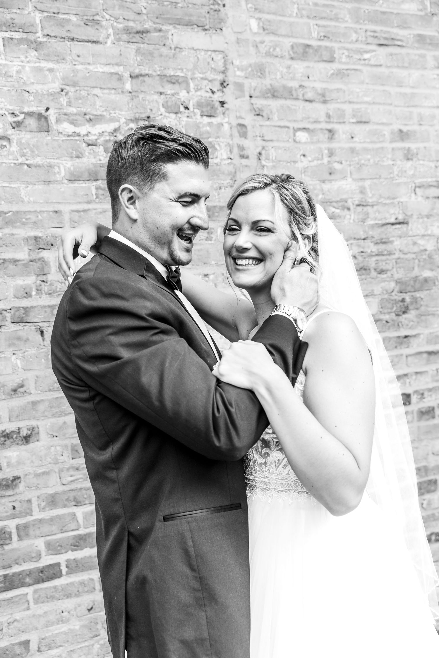 A bride and groom share a joyful candid moment together against a rustic brick wall.