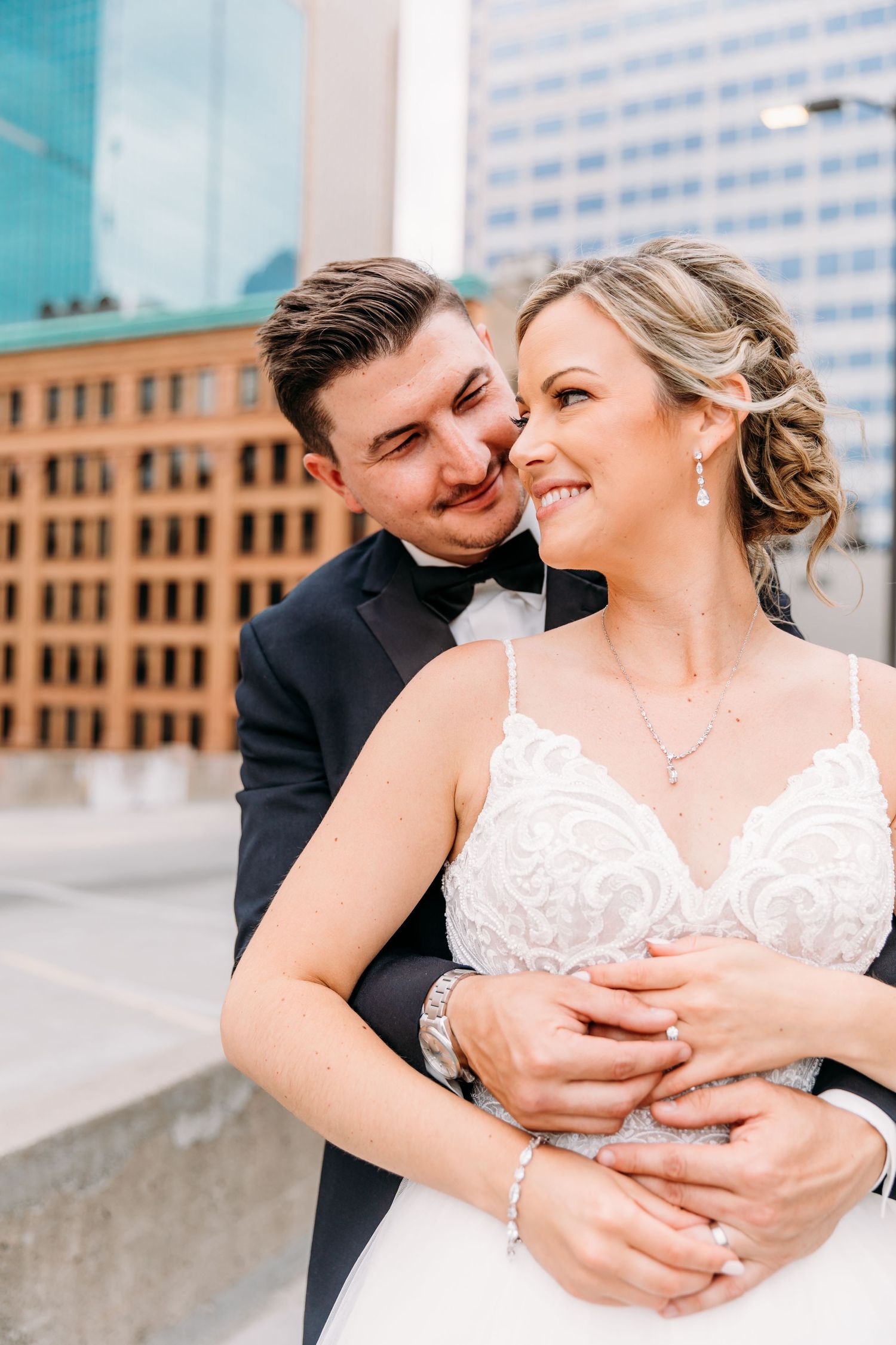 A romantic wedding couple embraces and shares intimate moments against an urban backdrop with brick buildings.
